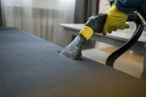 Man holding modern washing vacuum cleaner and cleaning dirty sofa with professionally detergent. Professional springclean at home concept